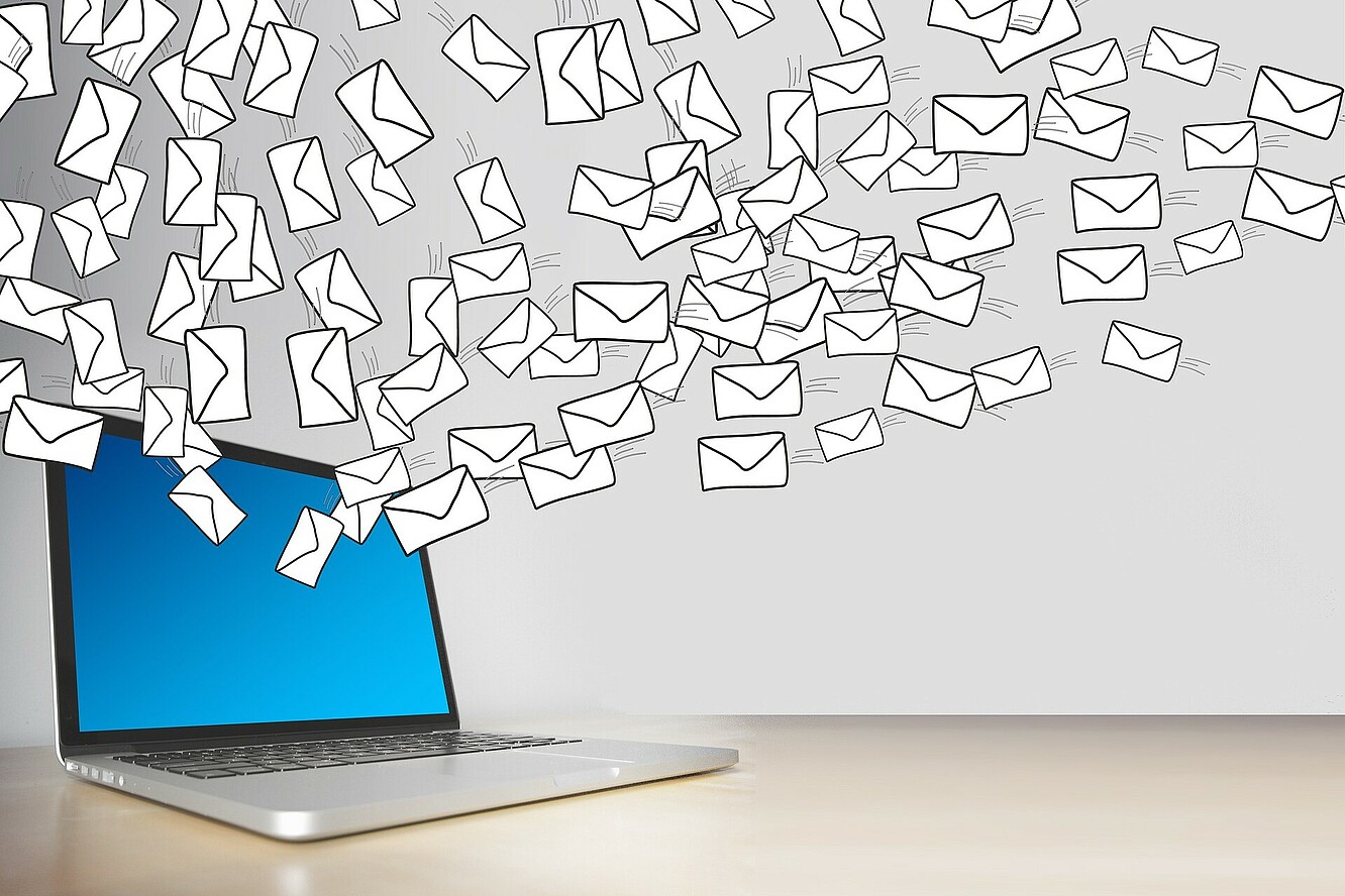 Bild auf dem ein Laptop zu sehen ist. Aus dem Laptop fliegen viele kleine weiße Briefumschläge, die E-Mail symbolisieren sollen. 
